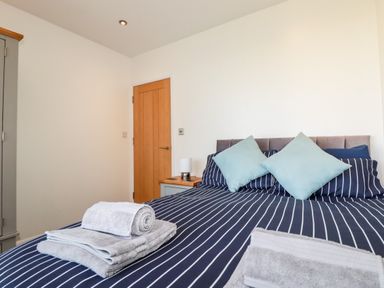 A bedroom with a bed with striped bedding pillows towels on bed a wooden door and a wardrobe at Seawynds in Crantock
