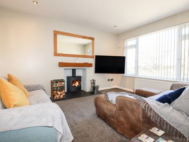 A living room with two sofas a fireplace a wall-mounted television and large windows at Seawynds in Crantock