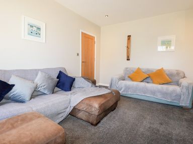 A living room with two sofas and cushions a wall clock and framed pictures at Seawynds in Crantock