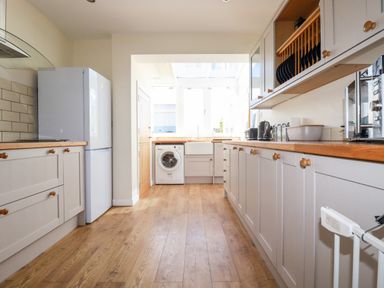 A kitchen with wooden floors white cabinets a refrigerator a washing machine and countertop appliances at Seawynds Crantock