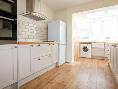 A kitchen with white cabinets a washing machine a refrigerator and a window at Seawynds in Crantock