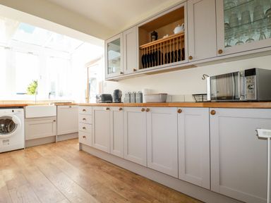 A kitchen with cabinets, wooden countertops, a washing machine, toaster, kettle, microwave, and dishes on racks at Seawynds in Crantock