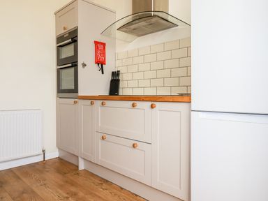 A kitchen with wooden floor white cabinets a double oven a knife block a fire blanket and a white refrigerator at Seawynds in Crantock