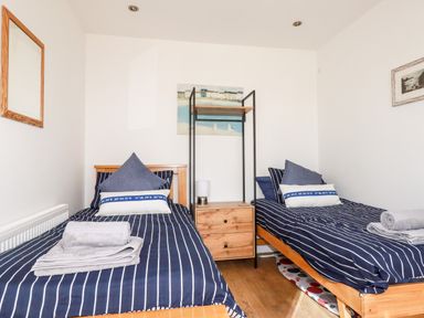 A bedroom with two single beds with striped bedding and pillows separated by a wooden nightstand with a lamp at Seawynds in Crantock