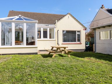 A backyard with a wooden picnic table lawn conservatory and house at Seawynds in Crantock