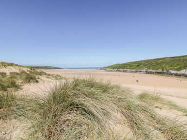 A sandy beach with grass-covered dunes and people walking near the water at Seawynds in Crantock
