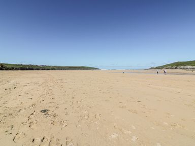 A wide sandy beach with footprints and few people walking near the shore at Seawynds in Crantock