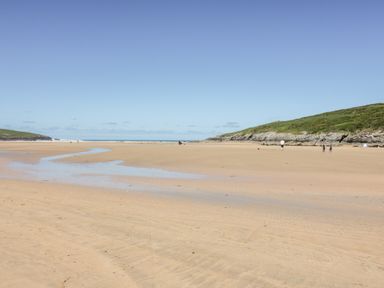 A sandy beach with a small stream and grassy cliffs in the background at Seawynds in Crantock