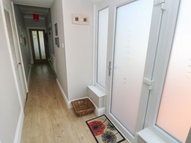 A hallway with wooden flooring a basket a mat and frosted glass door at Pinewood in Saundersfoot
