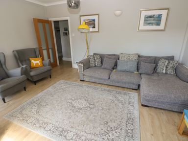 A living room with a gray sofa and armchairs a beige patterned rug a yellow floor lamp and framed pictures on the wall at Pinewood in Saundersfoot