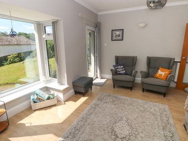 A sitting room with two armchairs with cushions a window with a view of a garden and a rug on the floor at Pinewood in Saundersfoot