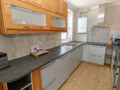 A kitchen with gray countertops wooden upper cabinets a sink stove and wooden floor at Pinewood in Saundersfoot