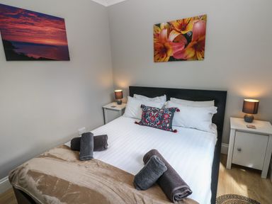 A bedroom with a bed with white sheets and towels on it two bedside tables with lamps and paintings on the walls at Pinewood in Saundersfoot