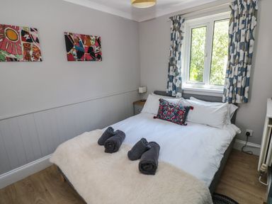 A bedroom with a bed with white sheets and a decorative pillow with blue curtains by the window at Pinewood in Saundersfoot