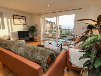 A living room with two leather sofas a coffee table and sliding glass doors leading to a balcony at A Stone's Throw in Downderry