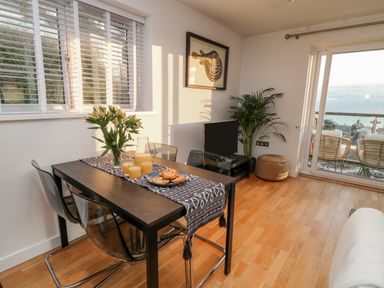 A dining area with a table set with juice and pastries next to a window and a balcony with chairs at A Stone's Throw in Downderry