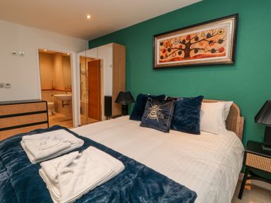 A bedroom with a bed with blue pillows and folded towels on it a dresser a wardrobe and an en suite bathroom at A Stone's Throw in Downderry