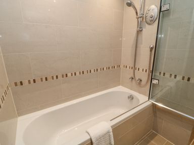 A bathroom with a bathtub shower and a towel at A Stone's Throw in Downderry