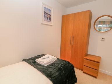 A bedroom with a wooden wardrobe a small wooden chest of drawers a bed with folded towels and a dark blanket at A Stone's Throw in Downderry