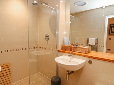 A bathroom with a walk-in shower, a sink with faucet, a mirror, and wicker baskets on a wooden shelf at A Stone's Throw in Downderry