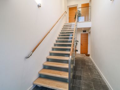 A hallway with a staircase featuring wooden steps and glass railing and wooden doors at A Stone's Throw in Downderry