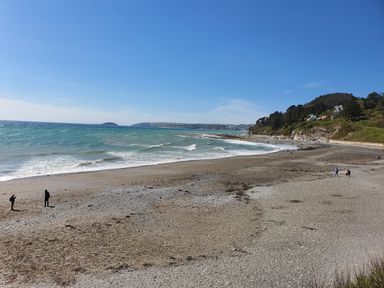 A beach with people walking near the shoreline and hills with houses in the background at A Stone's Throw in Downderry