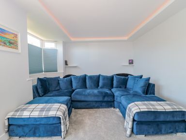 A living room with a blue sectional sofa and two plaid throws near a window with blinds at Fisherman's Rest in Wyke Regis