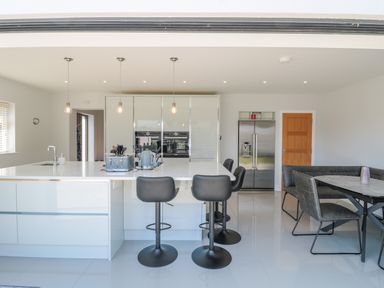 A modern kitchen with white cabinets black bar stools and a dining area at Fisherman's Rest in Wyke Regis