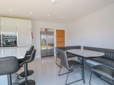 A kitchen with a refrigerator a kitchen island with black bar stools and a dining table with chairs and a bench at Fisherman's Rest in Wyke Regis