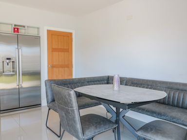A dining area with a round table and gray chairs next to a wooden door and stainless steel refrigerator at Fisherman's Rest in Wyke Regis