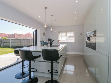 A kitchen with a large island counter and black stools next to an open door to a garden at Fisherman's Rest in Wyke Regis