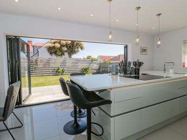 A kitchen with a countertop island bar stools hanging lights and opens to a garden at Fisherman's Rest in Wyke Regis
