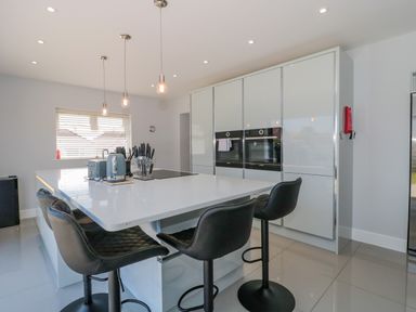 A modern kitchen with a large island and black bar stools at Fisherman's Rest in Wyke Regis