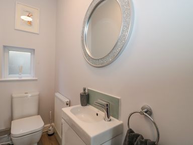 A bathroom with a toilet a sink with a soap dispenser a round mirror and a towel on a ring at Fisherman's Rest in Wyke Regis