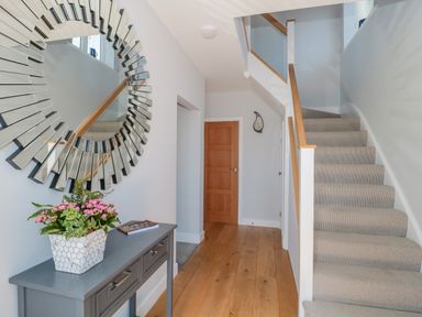 A hallway with wooden floor a gray console table with flowers a round mirror and carpeted stairs at Fisherman's Rest in Wyke Regis