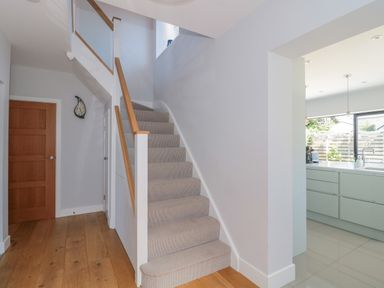 A staircase with carpeted steps and wooden handrails next to a wooden door and an open doorway to a kitchen area at Fisherman's Rest in Wyke Regis