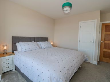 A bedroom with a double bed white bedding two bedside tables lamps two doors and a ceiling light at Fisherman's Rest in Wyke Regis