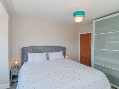 A bedroom with a king size bed two bedside tables lamps a wooden door and a frosted glass sliding wardrobe door at Fisherman's Rest in Wyke Regis