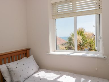 A bedroom with a wooden bed frame white bedding near a window showing outdoor plants and a roof at Fisherman's Rest in Wyke Regis