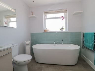 A bathroom with a freestanding bathtub a toilet a window and a towel rack at Fisherman's Rest in Wyke Regis