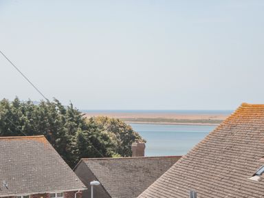 A view of rooftops trees and a body of water with a sandy shore in the distance at Fisherman's Rest in Wyke Regis