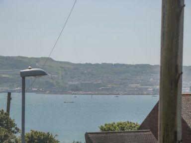 A coastal view with water boats and buildings on a hillside with a streetlight and rooftops in the foreground at Fisherman's Rest in Wyke Regis