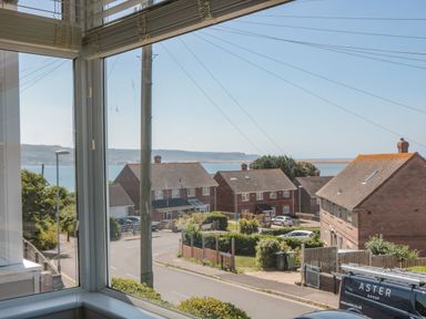 A view through a corner window of a street with houses cars and the sea in the background at Fisherman's Rest in Wyke Regis