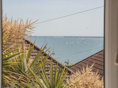 A sea view with sailboats and rooftops seen through plants at Fisherman's Rest in Wyke Regis