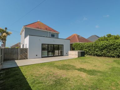 A backyard with a grassy lawn a tiled patio fence and a two story house at Fisherman's Rest in Wyke Regis