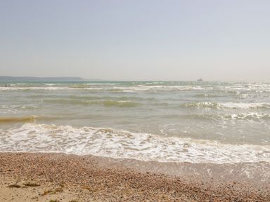 A pebble beach with waves and a distant ship on the sea at Fisherman's Rest in Wyke Regis