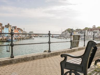A waterfront promenade with a bench railing and boats docked along a harbor at Fisherman's Rest in Wyke Regis