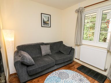 A living room with a grey sofa three cushions a floor lamp round rug and a window at Honeysuckle Cottage in Crossgates