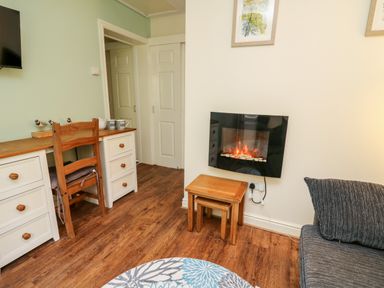 A room with a wooden desk and chair a wall-mounted electric fireplace and a small wooden table at Honeysuckle Cottage in Crossgates