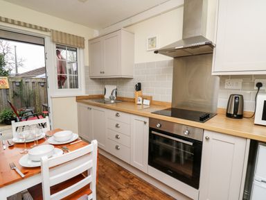A kitchen with white cabinets a stove a kettle and a dining table set for two at Honeysuckle Cottage in Crossgates